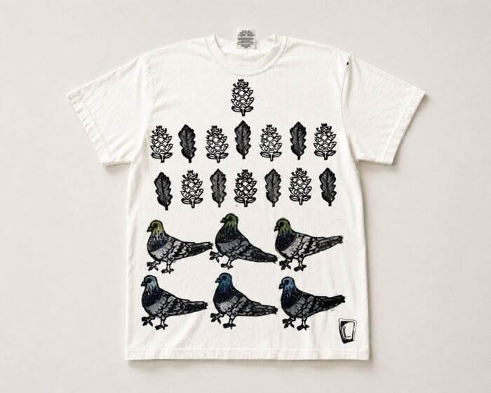 White tee hand printed with rows of pinecones and leaves above six pigeons