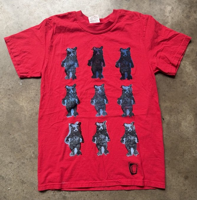 Red tee hand printed with nine blue and black raccoons standing in rows